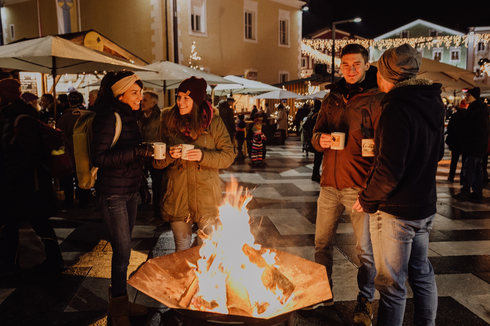 Vier Personen die um einen Feuerkorb am Adventmarkt in Mondsee stehen.